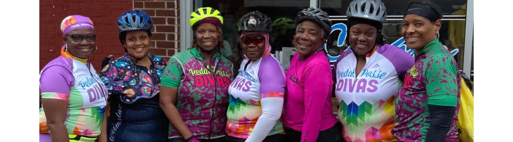 Happy riders with and without bikes smile in front of a sculpture of a bear. 